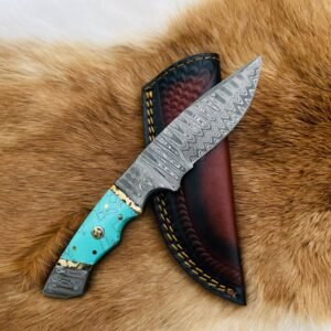A Damascus steel knife with a turquoise handle and gold pins, resting on a brown fur background beside a dark leather sheath