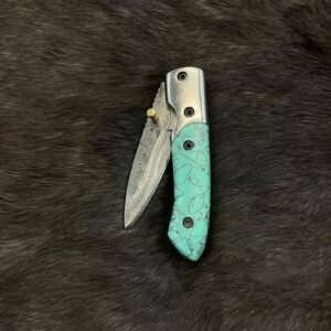 A folding knife with a Damascus steel blade and a turquoise-colored handle, partially open on a dark textured surface