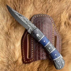A folding knife with a patterned Damascus steel blade and blue and gray handle rests on a brown leather sheath over fur