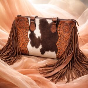 A Western-style handbag with a brown and white cowhide body, floral tooled leather sides with studs, and long brown fringes
