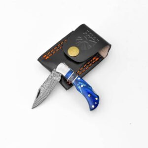 An open folding knife with a blue marbled handle and a patterned blade next to a black leather pouch with orange stitching and a brass button