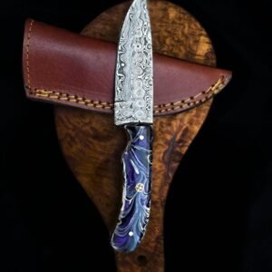 A custom knife with a patterned Damascus blade and a purple-marbled handle, resting on a brown leather sheath and dark wood