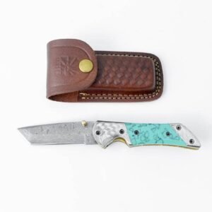 A folding knife with a Damascus blade and turquoise-patterned handle with silver eagle details, next to a brown leather sheath
