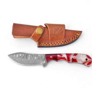 A Damascus steel knife with a wavy blade and a red and white marbled handle rests beside its brown leather sheath