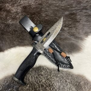 A Damascus steel knife with a patterned blade, cutouts, and a dark handle rests in an ornate black leather sheath on a fur surface