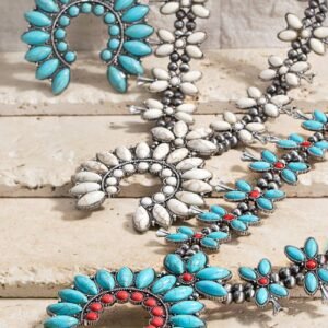 Close-up of three Southwestern squash blossom necklaces with turquoise, white, and coral-red stones on a textured surface