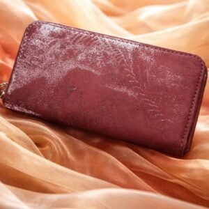 A dark red rectangular wallet with a textured, slightly sparkly surface sits on flowing peach fabric