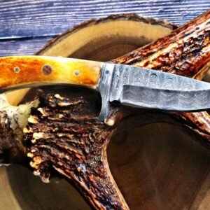 Knife with a patterned Damascus steel blade and an orange-yellow antler handle, resting on a deer antler
