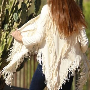 A woman from behind wears a cream fringed jacket and dark jeans, with long reddish-brown hair, next to a cactus
