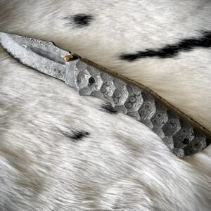 A folding knife with a swirling Damascus steel pattern on its blade and textured handle, lying on white fur