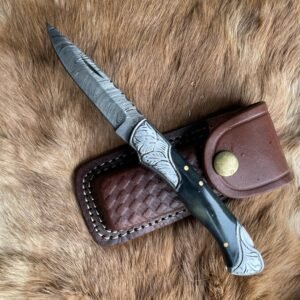 A custom knife with a Damascus blade and dark, silver-accented handle rests on brown fur next to a leather sheath