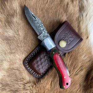 A folding knife with a wavy Damascus blade and a multicolored handle, next to a "Titan" leather sheath on brown fur