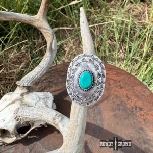 A silver oval ring with a turquoise stone and stamped patterns rests on a deer antler, with a Rowdy Crowd logo in the corner
