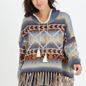 A smiling woman wears a blue, brown, and tan Southwestern-patterned hooded sweater with tassels and a fringed hem
