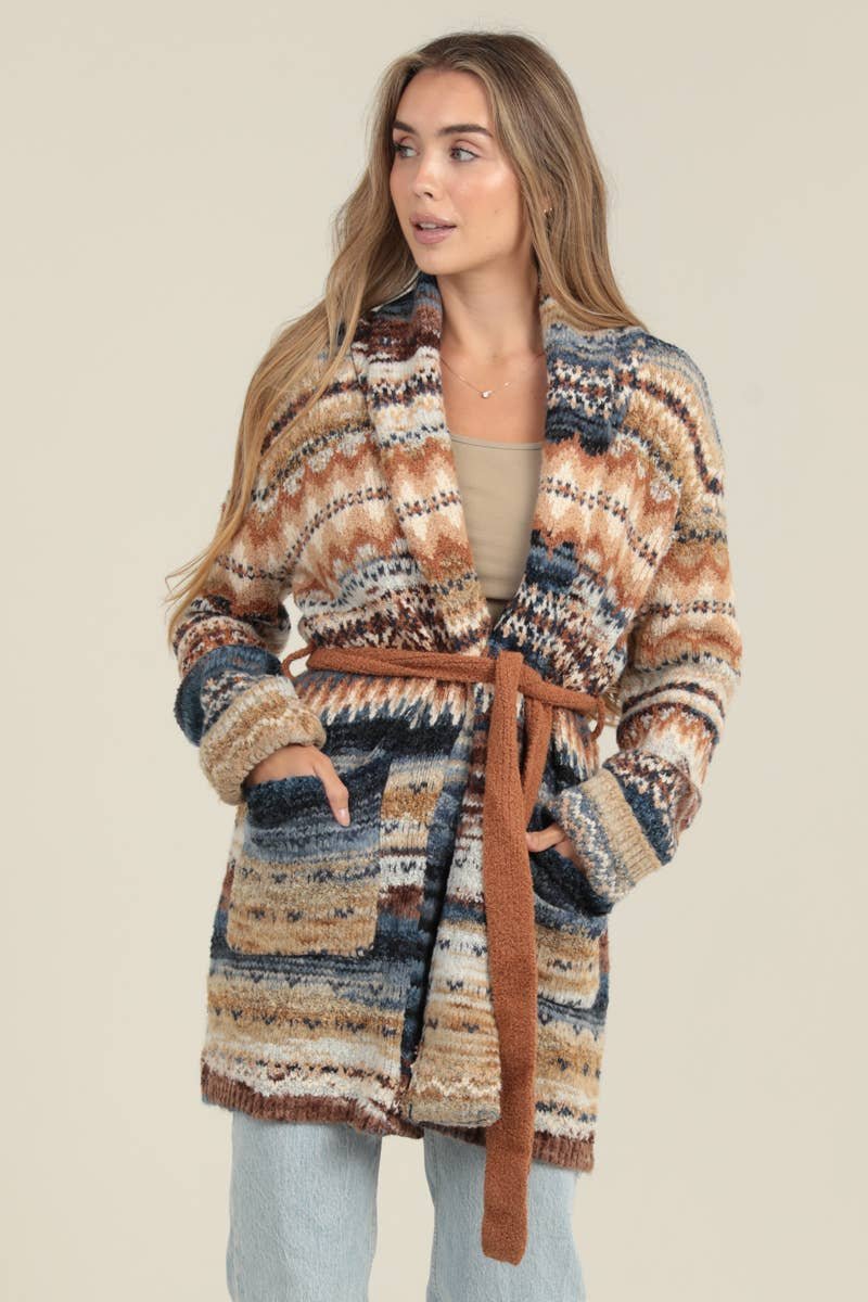 A woman wearing a cozy patterned cardigan in shades of blue, brown, tan, and cream, tied with a soft brown belt