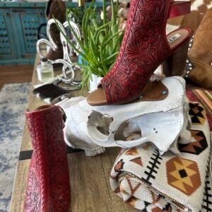 A pair of red carved leather open-toe boots displayed on a white animal skull and a patterned blanket
