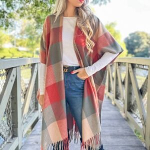 A woman in a hat and blue mirrored sunglasses, wearing a plaid poncho over a white shirt and jeans, stands on a wooden bridge