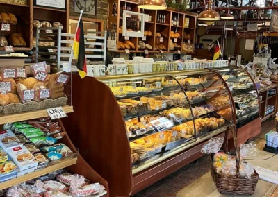 Interior of a German bakery featuring a long display case filled with pastries, shelves of bread, and a "Willkommen" sign