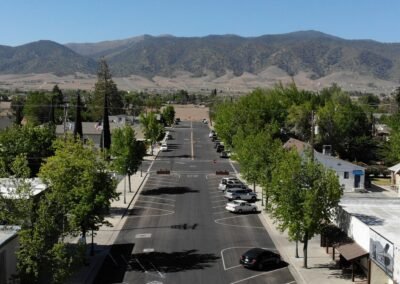 An aerial view of a tree-lined street with parked cars and "STOP" markings, leading to a distant mountain range