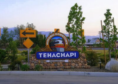 A decorative stone sign for 'Tehachapi Historic Downtown' features a train emblem and a left-pointing arrow, with mountains behind it